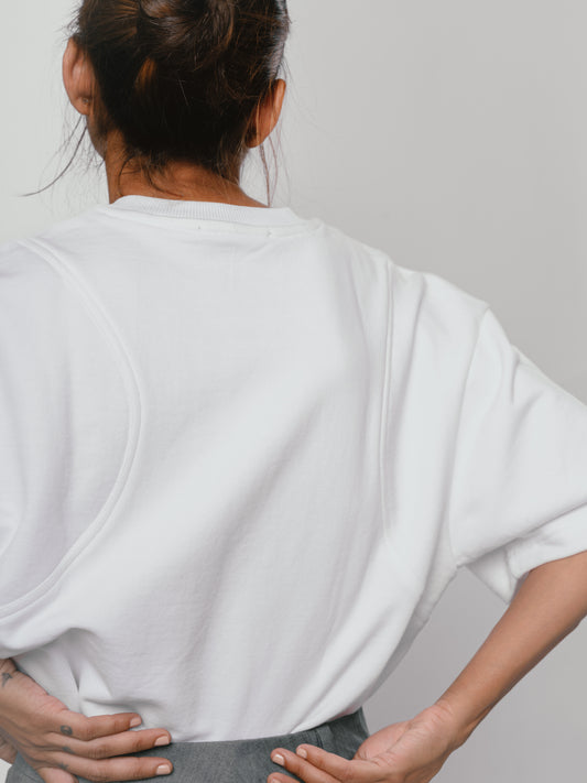 Person wearing a white oversized t-shirt against a plain background, seam contouring detail at the back